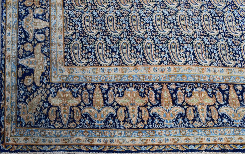 A vintage Persian Kerman rug featuring a deep blue field with intricate paisley and floral motifs.