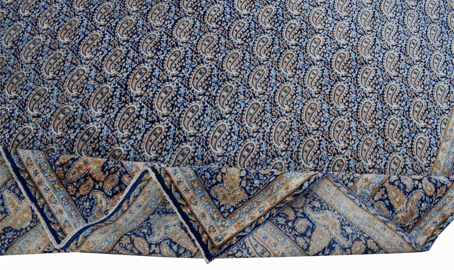 A vintage Persian Kerman rug featuring a dense blue paisley pattern and a decorative border.