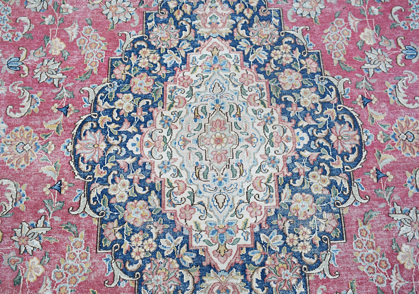 A vintage Persian Kerman rug featuring an intricate floral medallion on a pink and blue field.