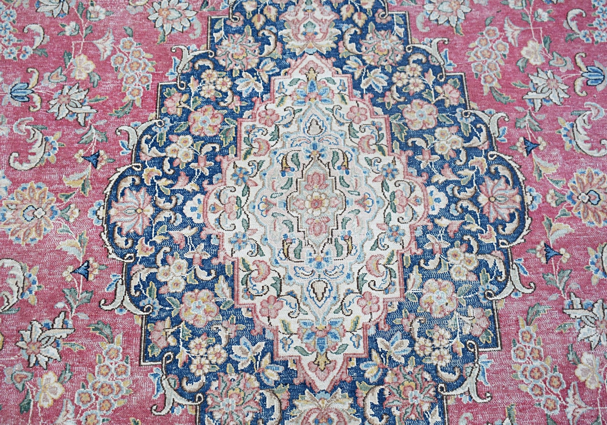 A vintage Persian Kerman rug featuring an intricate floral medallion on a pink and blue field.