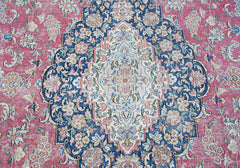 A vintage Persian Kerman rug featuring an intricate floral medallion on a pink and blue field.