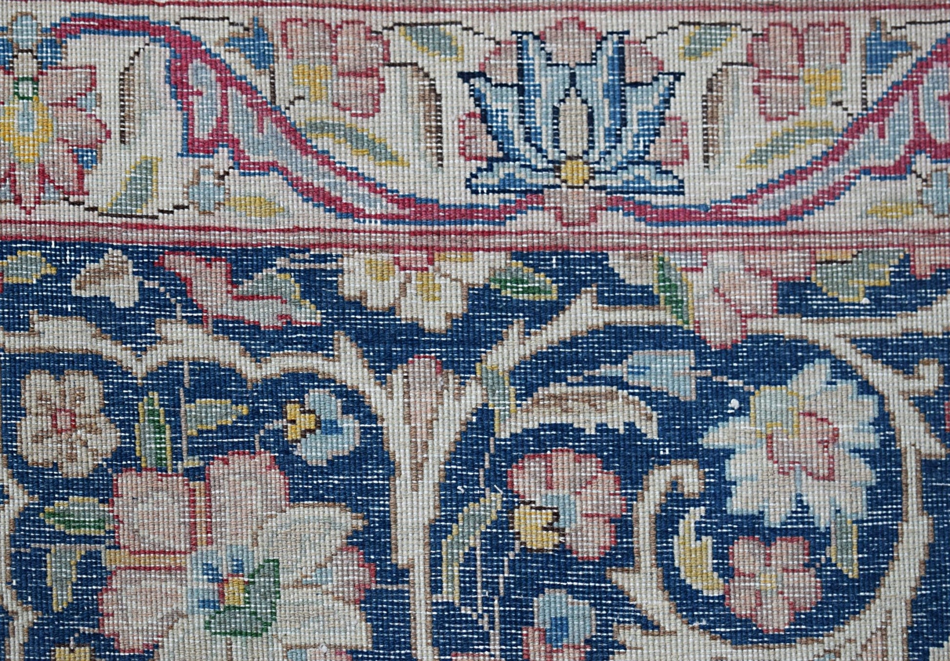 A close-up of a vintage Persian Kerman rug featuring intricate floral patterns on a blue field.