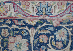 A close-up of a vintage Persian Kerman rug featuring intricate floral patterns on a blue field.