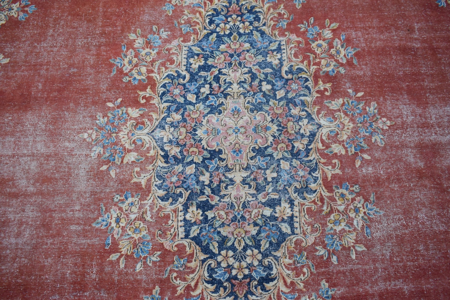A vintage Persian Kerman rug featuring a central floral medallion on a distressed red background.