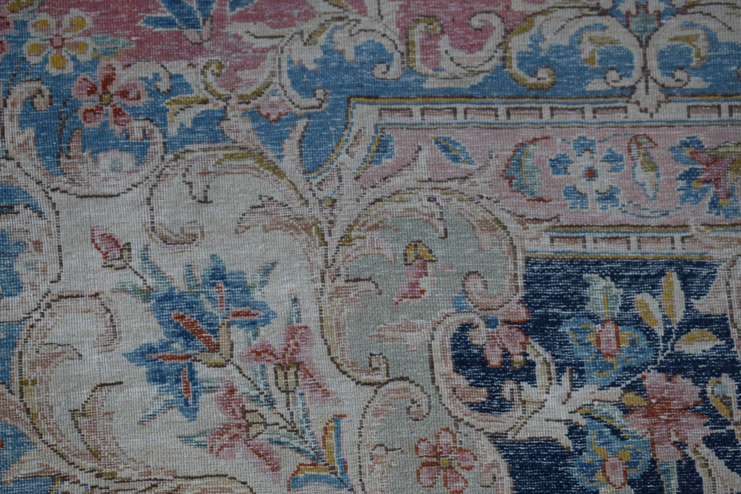 A close-up of a vintage Persian Kerman rug featuring intricate floral patterns in soft colors.
