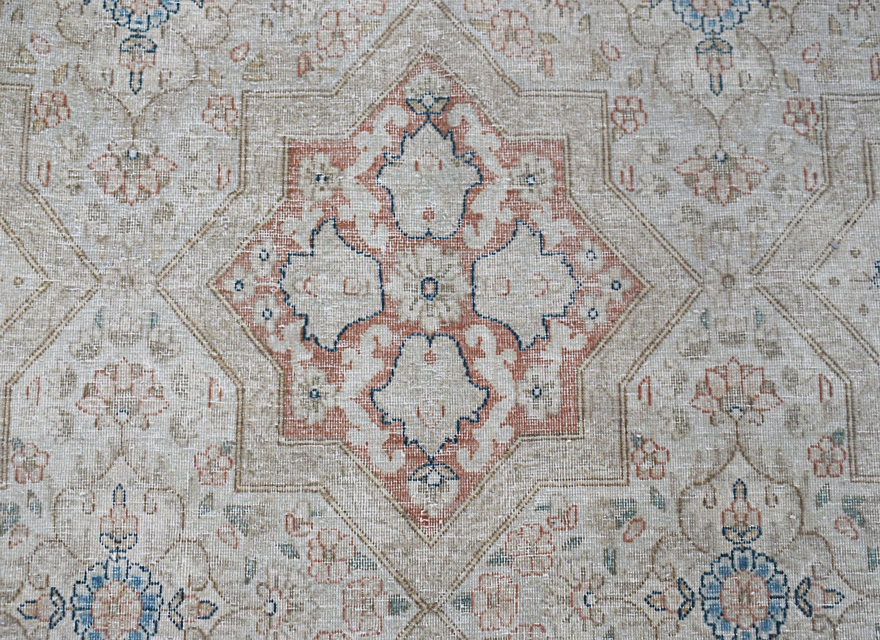 A vintage Persian Kerman rug featuring a central floral medallion in soft blue and terracotta tones.