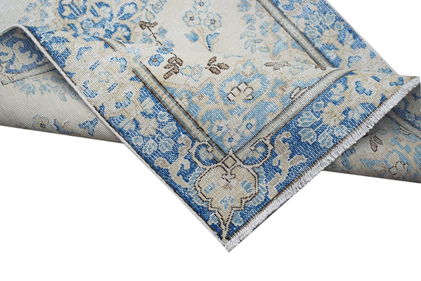 A vintage Persian Kerman runner featuring a blue and cream floral pattern with a folded corner.