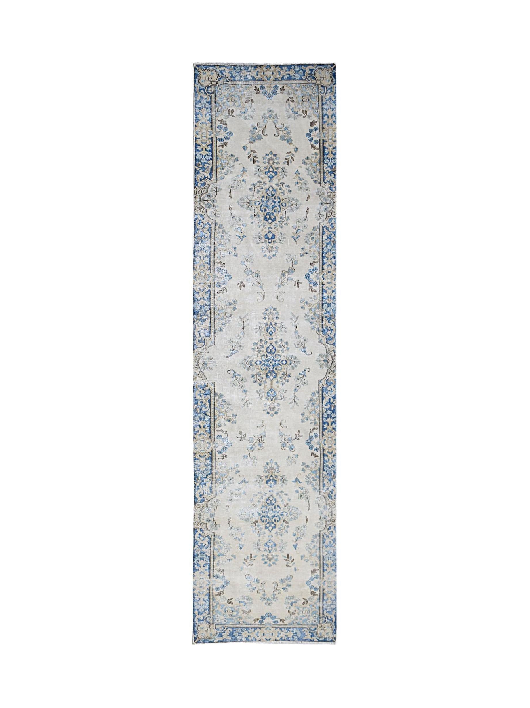 A vintage Persian Kerman runner rug featuring a blue floral medallion pattern on a cream background.