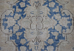 A vintage Persian Kerman runner featuring a central floral medallion in blue on a beige field.