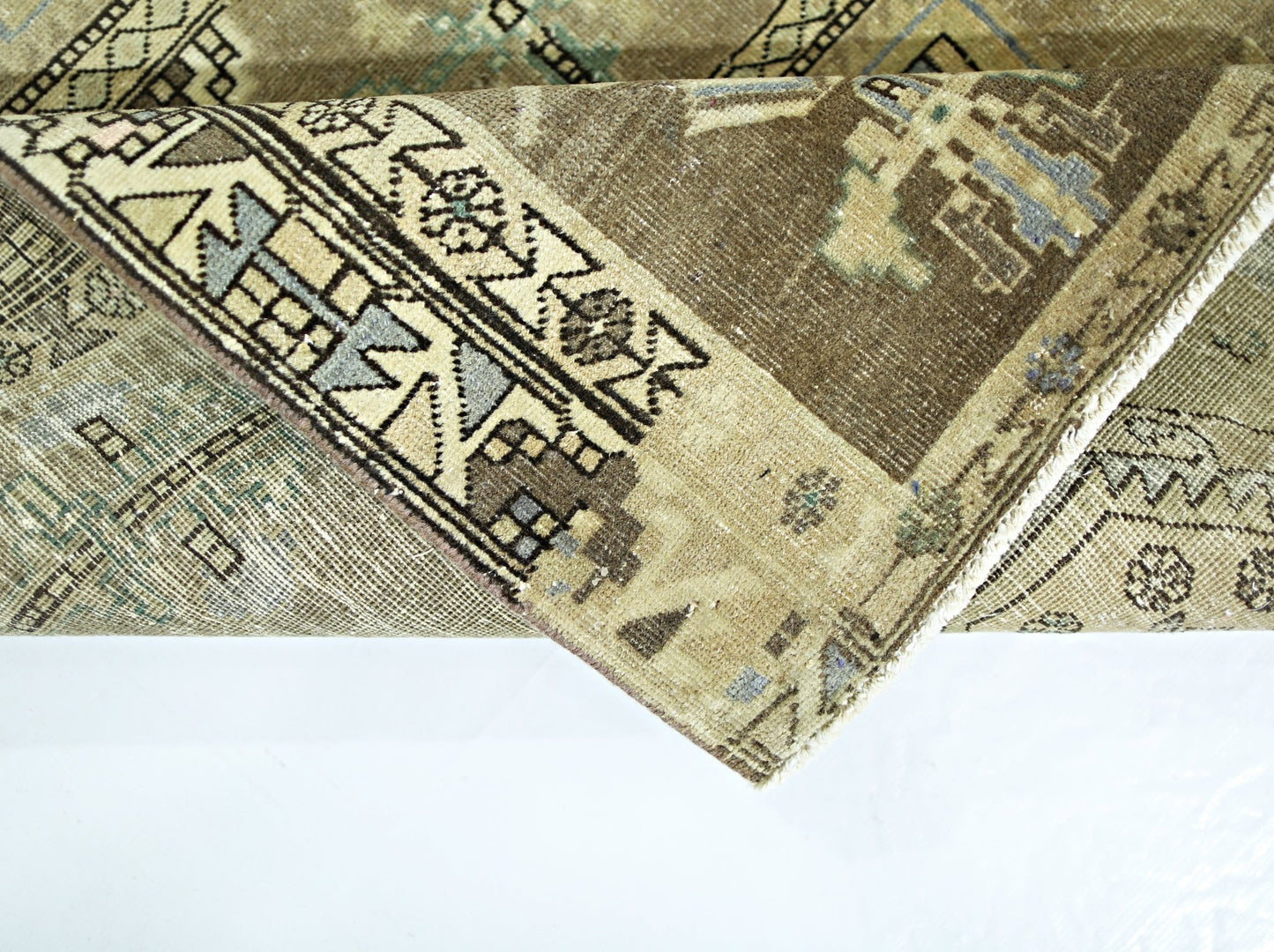 A folded vintage Persian rug featuring intricate geometric patterns in muted brown and blue tones.