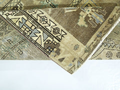 A folded vintage Persian rug featuring intricate geometric patterns in muted brown and blue tones.