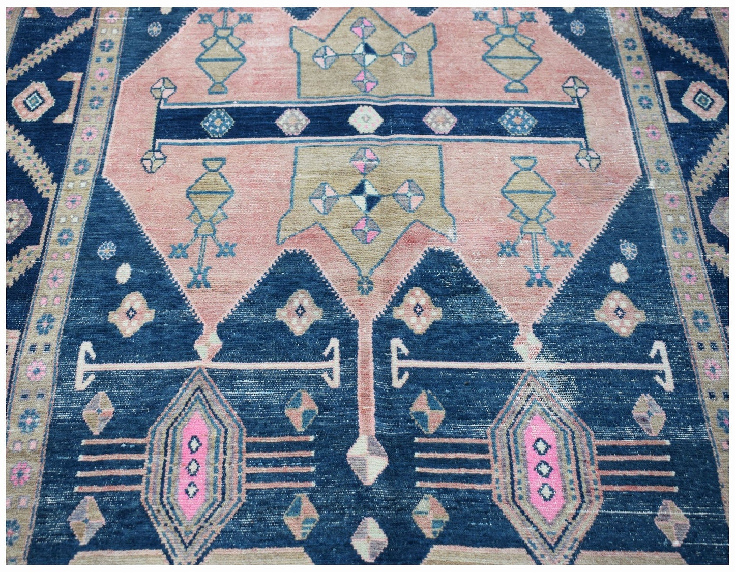 A vintage handwoven Persian Koliai rug featuring geometric patterns in blue, pink, and tan.