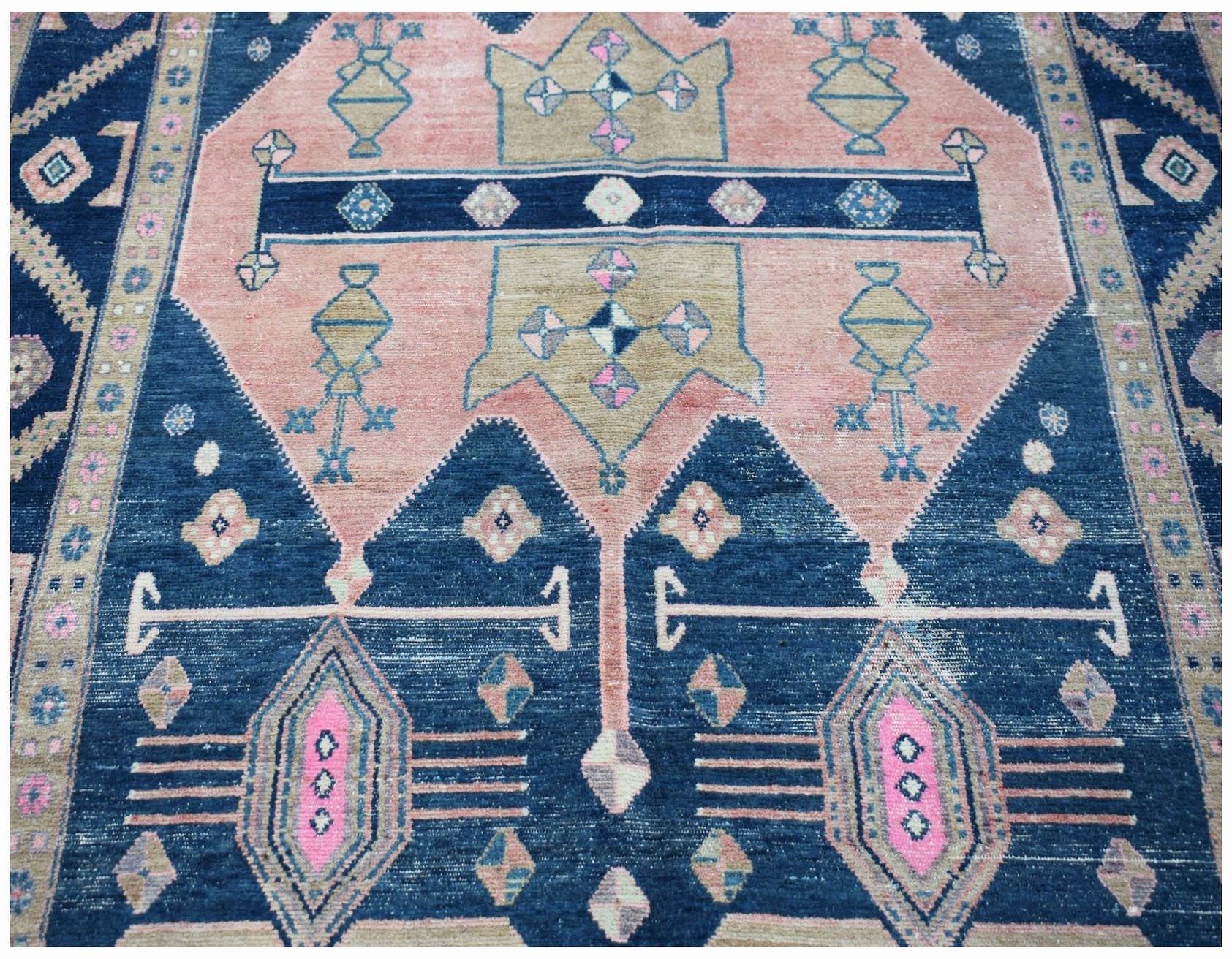 A vintage handwoven Persian Koliai rug featuring geometric patterns in blue, pink, and tan.