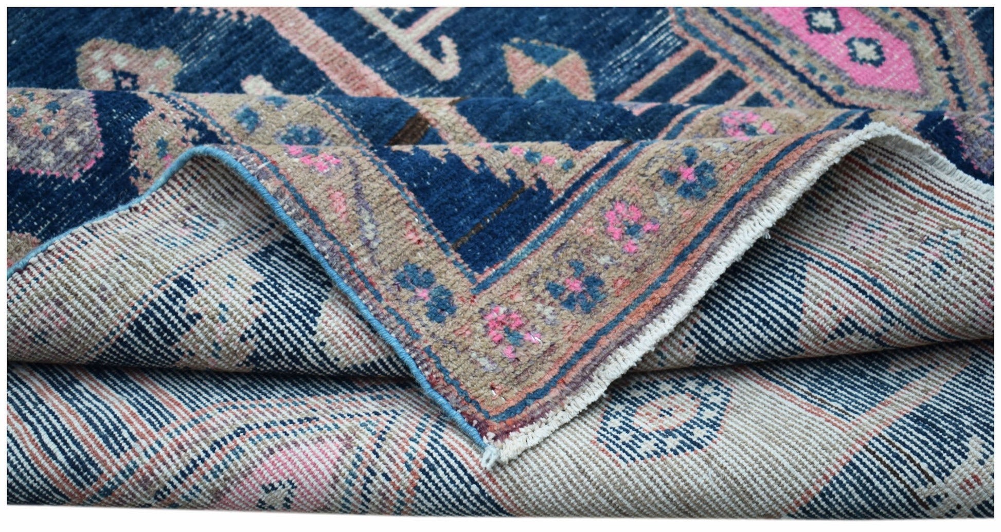 A folded vintage Persian Koliai rug featuring a blue and tan floral pattern on a wool pile.