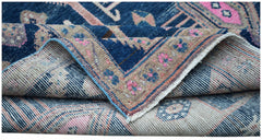 A folded vintage Persian Koliai rug featuring a blue and tan floral pattern on a wool pile.
