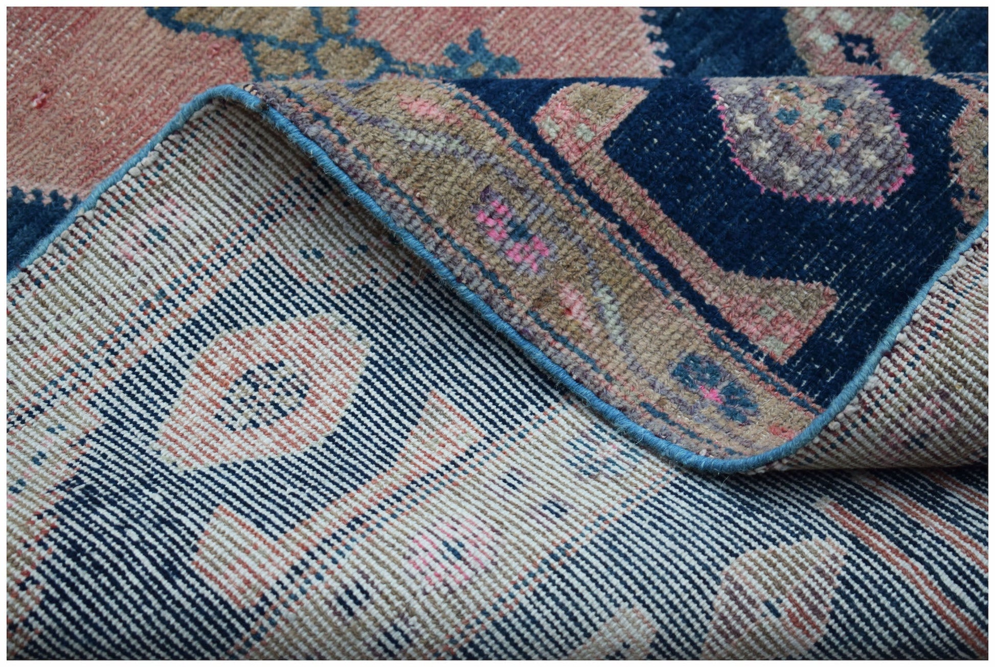 A corner of a vintage Persian Koliai rug is folded back to show its handwoven wool construction.