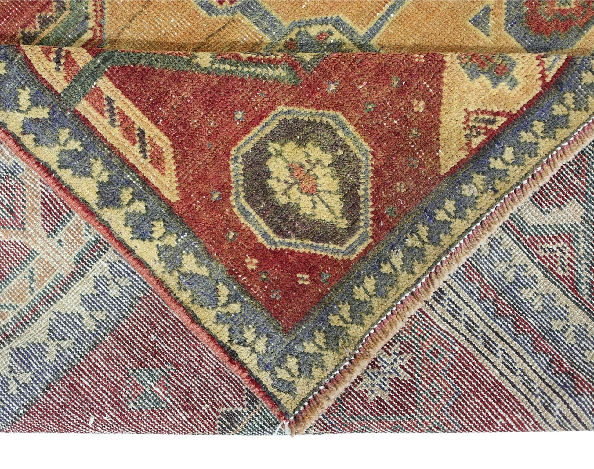A corner of a vintage Persian rug showing a red field with floral motifs and a blue border.