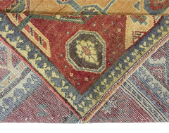 A corner of a vintage Persian rug showing a red field with floral motifs and a blue border.
