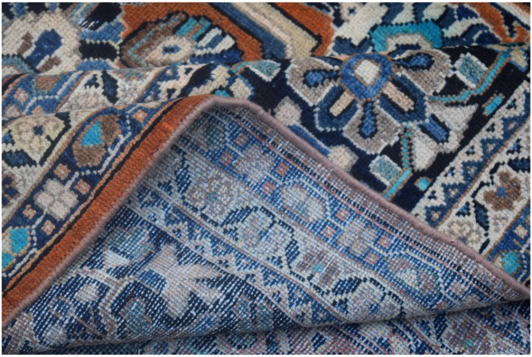 A corner of a vintage Persian Lori rug is folded back to show its intricate blue wool weave.