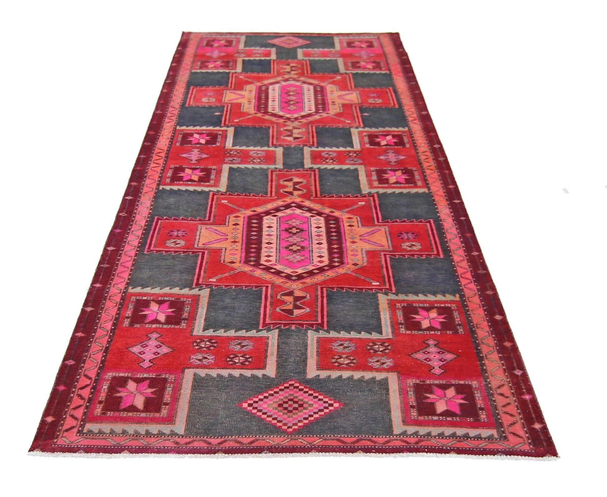 A handmade vintage Persian runner rug featuring geometric patterns in red, pink, and dark grey.