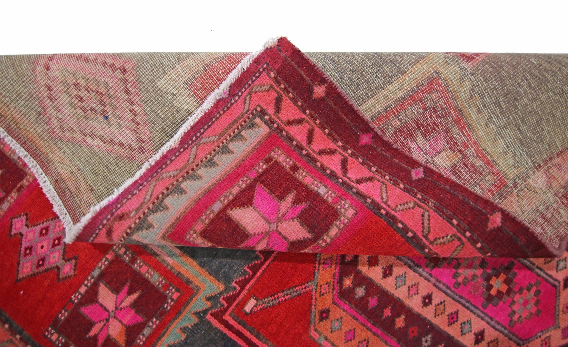 A vintage Persian rug with geometric patterns in shades of red, pink, and grey.