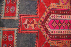 A vintage Persian rug featuring geometric patterns in shades of red, pink, and dark grey.