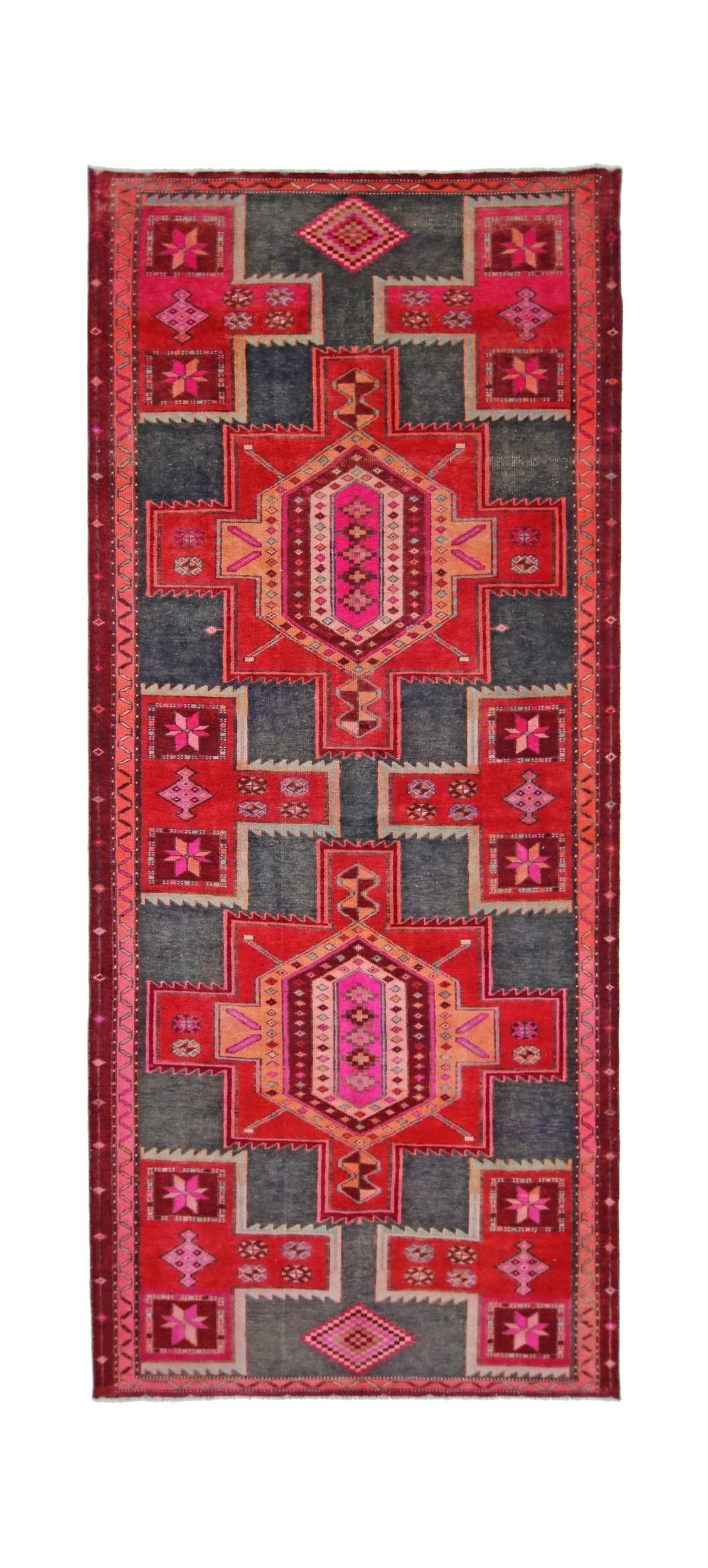 A handmade vintage Persian rug featuring geometric patterns in vibrant red, pink, and dark grey.
