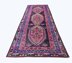 A vintage Persian Lori runner featuring geometric medallions in vibrant pink and dark charcoal.