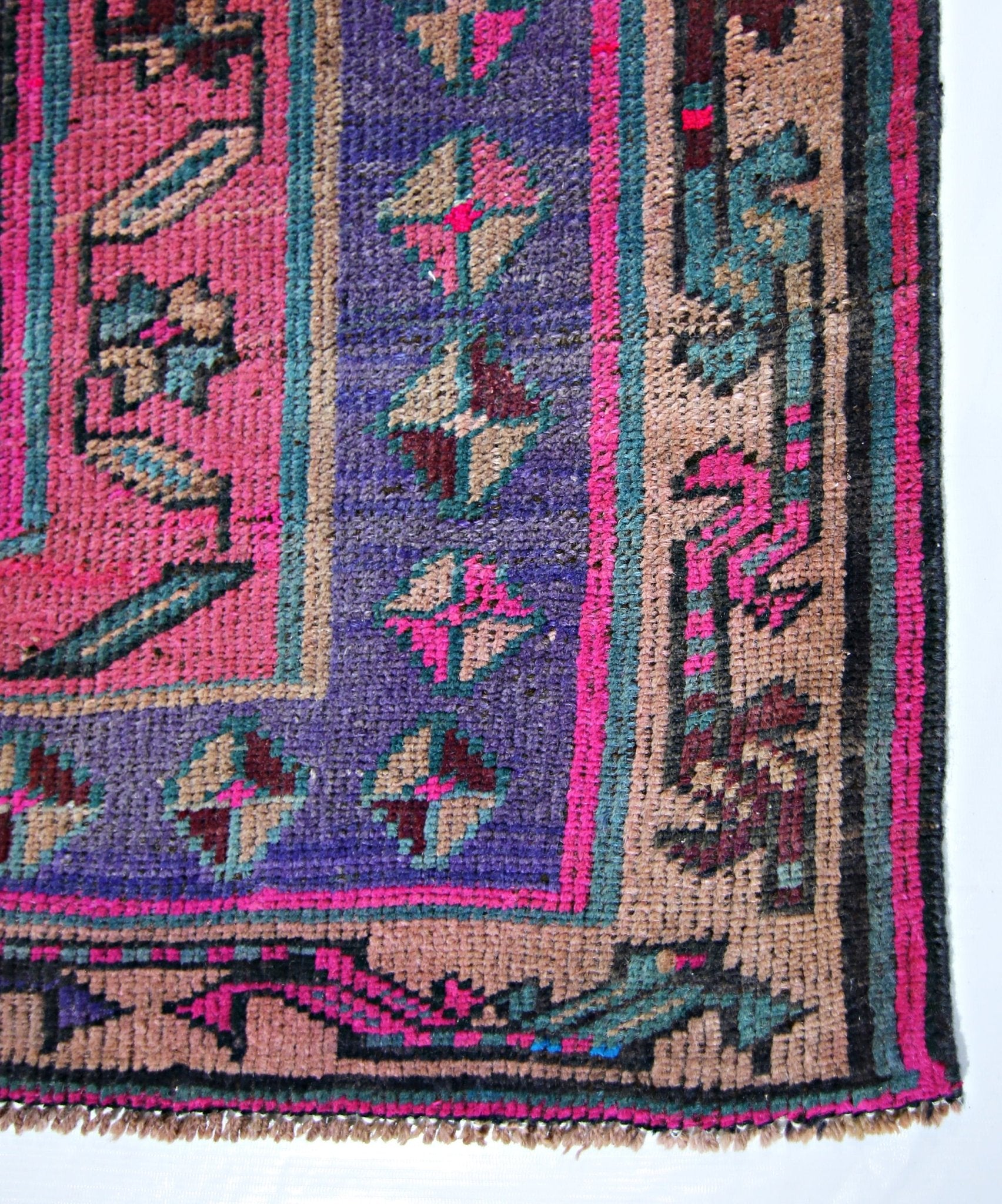 A vintage Persian Lori runner featuring a vibrant geometric pattern in pink, purple, and tan.