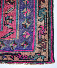 A vintage Persian Lori runner featuring a vibrant geometric pattern in pink, purple, and tan.