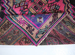 A vintage Persian Lori runner featuring a vibrant geometric pattern in pink, blue, and brown.