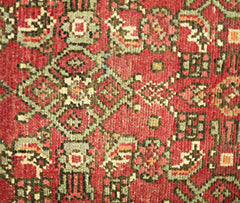 A close-up of a vintage Persian Hamadan runner featuring intricate geometric patterns in red and green.