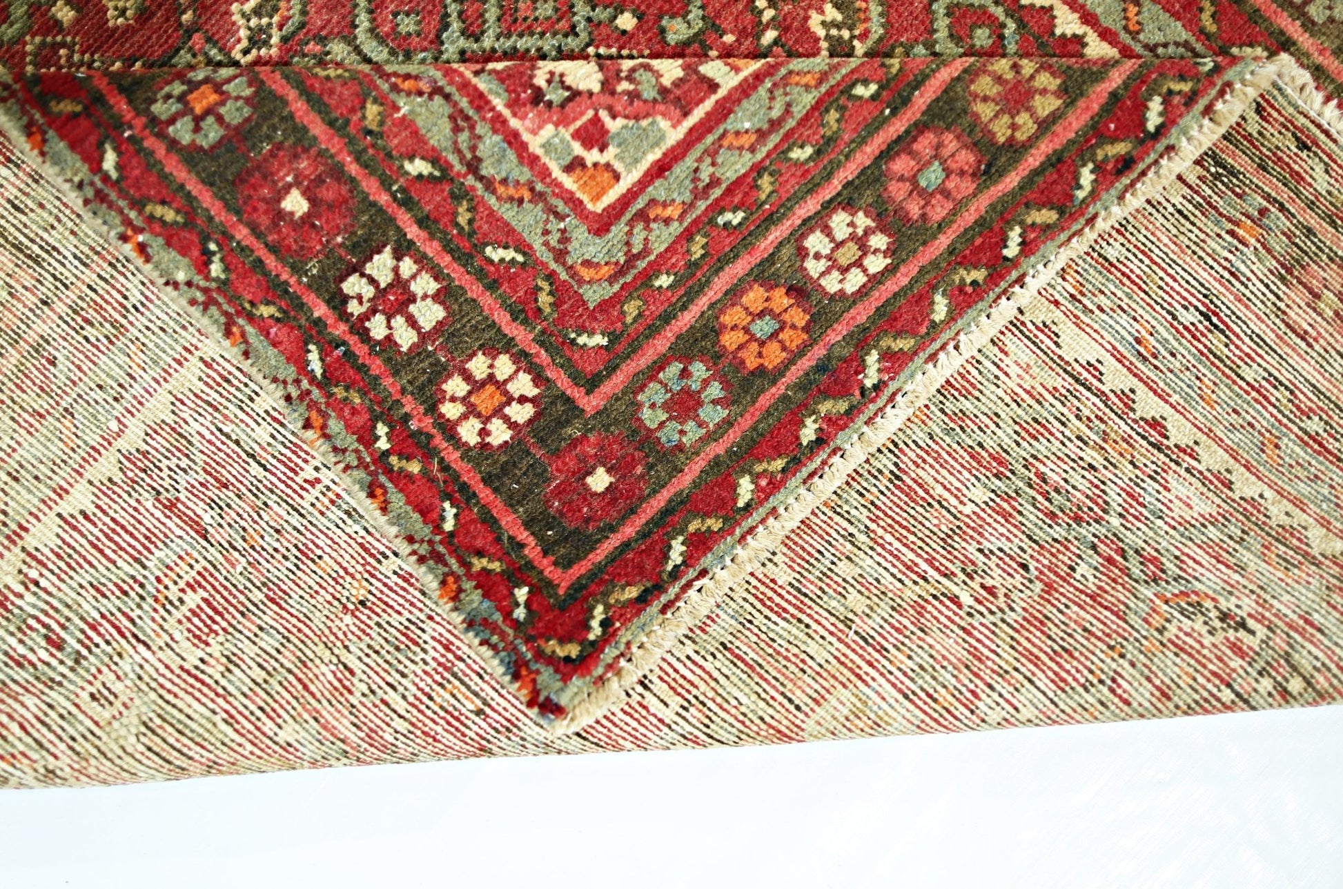 A corner of a vintage Persian Hamadan runner showing its intricate red and green wool pattern.