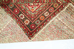 A corner of a vintage Persian Hamadan runner showing its intricate red and green wool pattern.