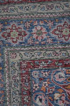 A vintage Persian Mashad rug featuring intricate floral patterns in blue, red, and orange tones.