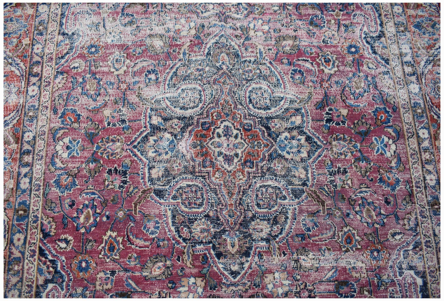 A vintage Persian Mashhad rug featuring a central floral medallion in shades of red and blue.