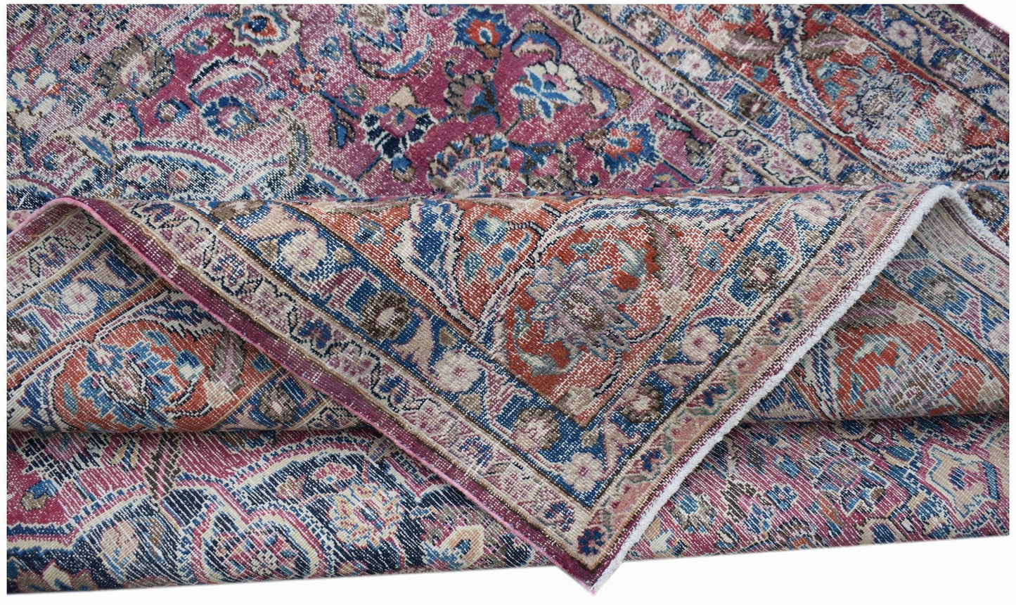 A vintage handwoven Persian Mashhad rug featuring intricate floral patterns in pink and blue tones.