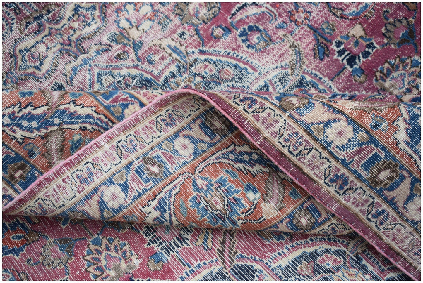A vintage Persian Mashhad rug featuring intricate floral patterns in shades of pink, blue, and tan.