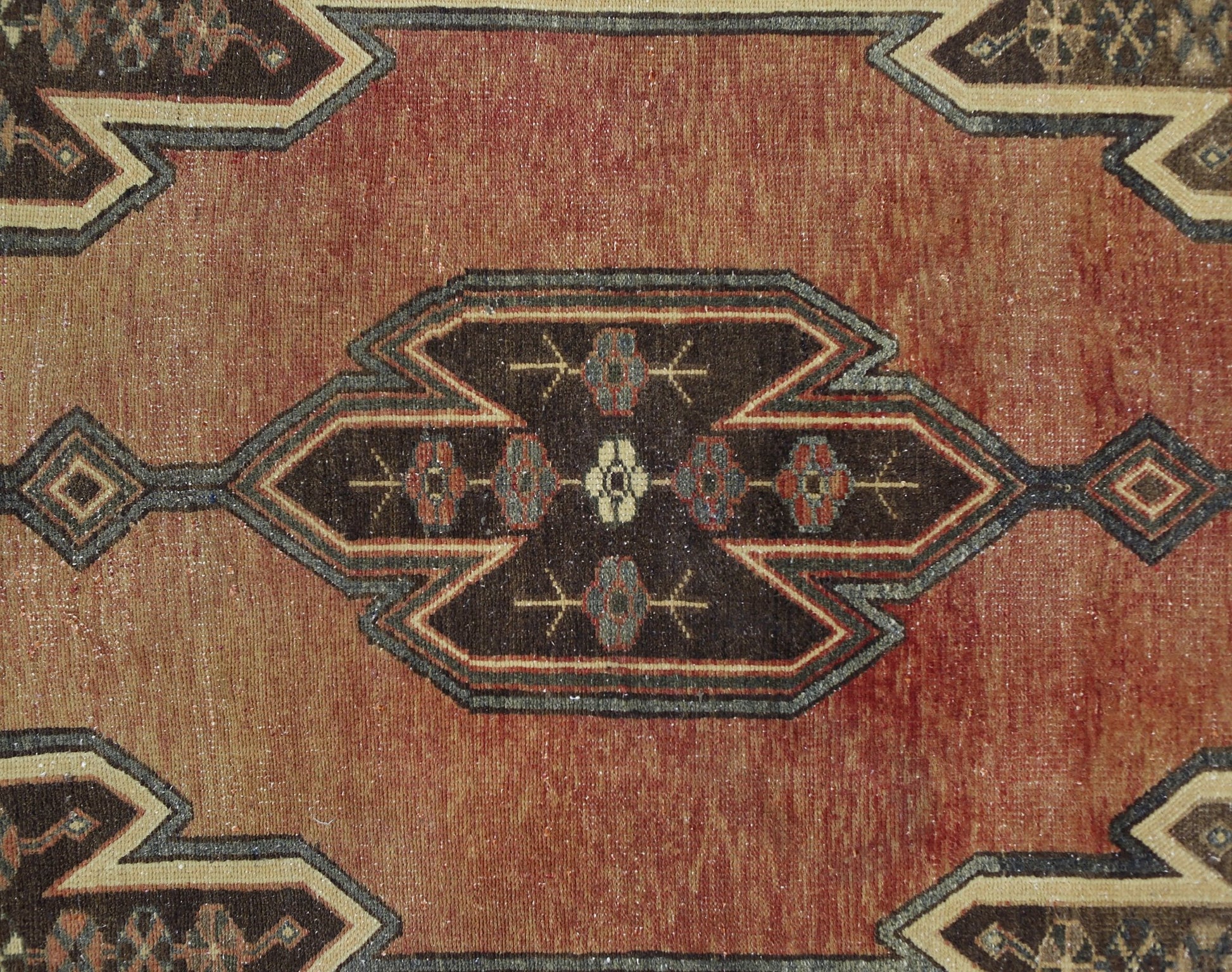 A vintage Persian Mazlaghan rug featuring a geometric medallion pattern in rust and dark brown.