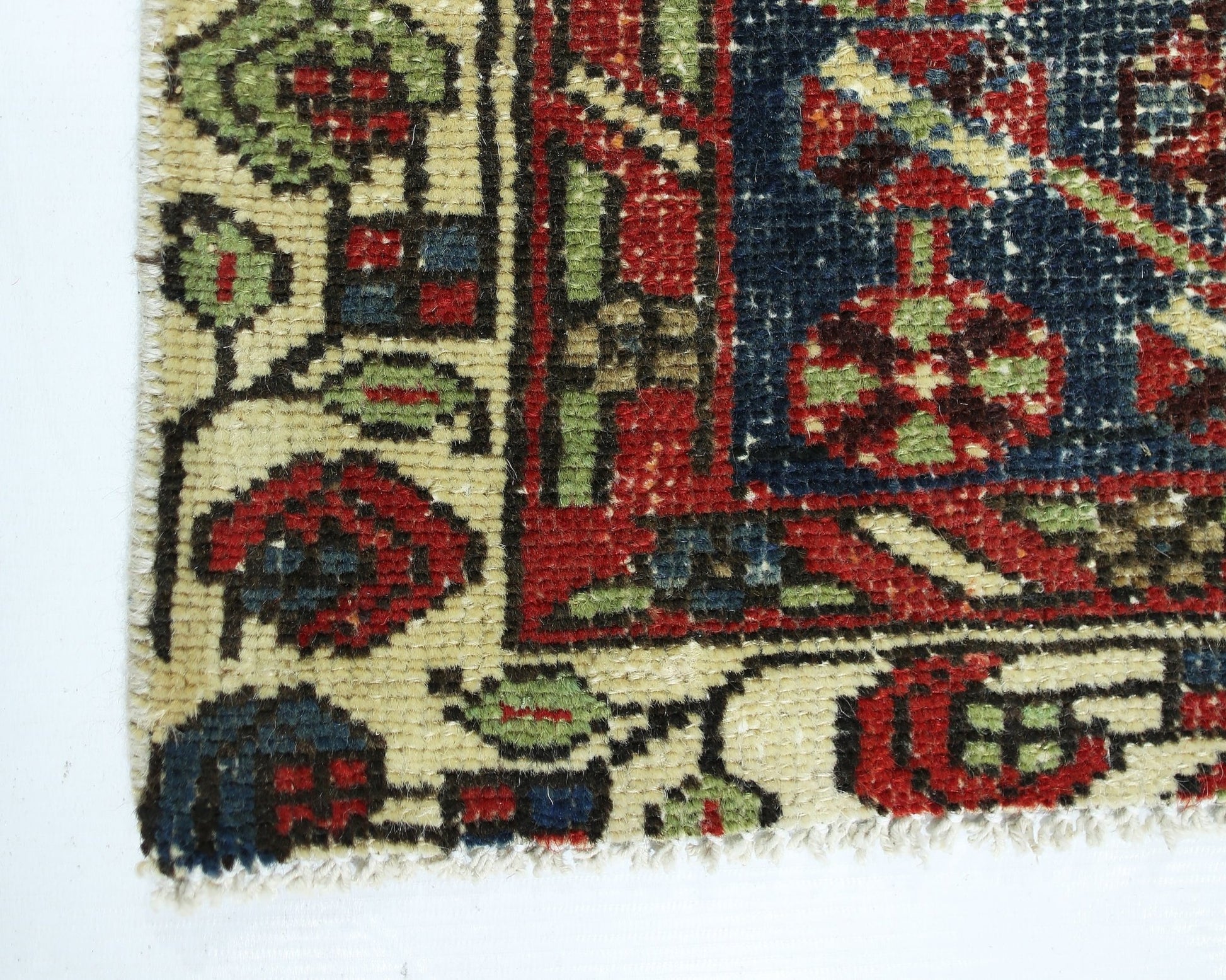 A corner view of a vintage Persian Mazlaghan rug featuring geometric floral patterns in red, blue, and green on a cream background.