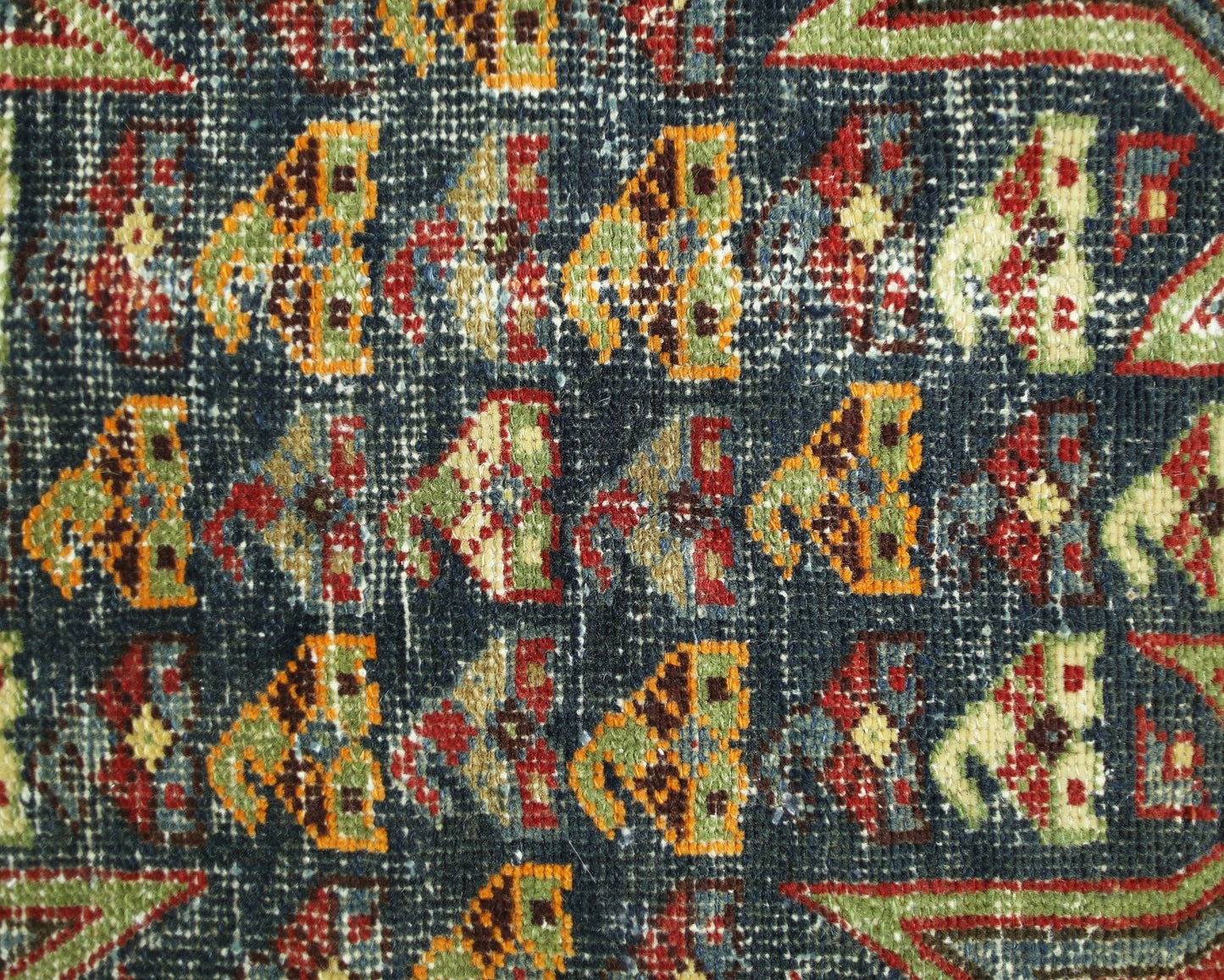 A close-up of a vintage Persian Mazlaghan rug featuring a repeating geometric pattern in wool.