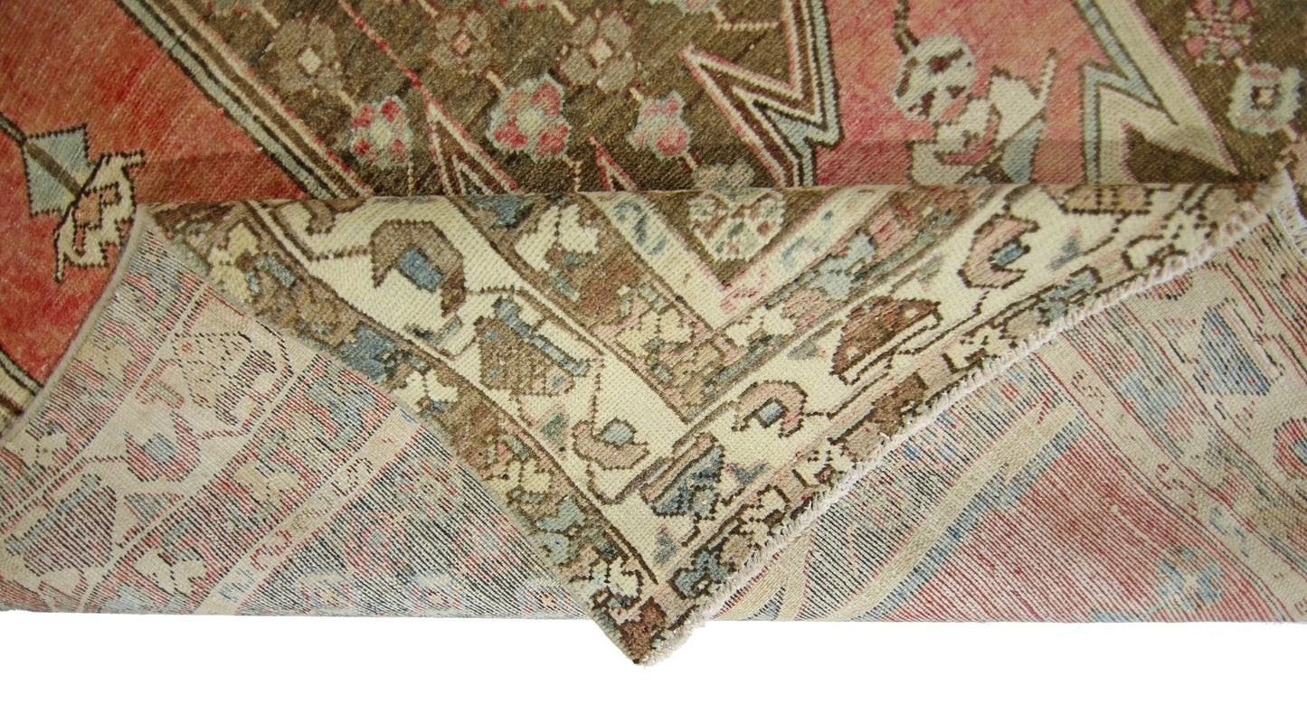 A vintage Persian Mazlaghan rug with a folded corner revealing its intricate wool pattern.
