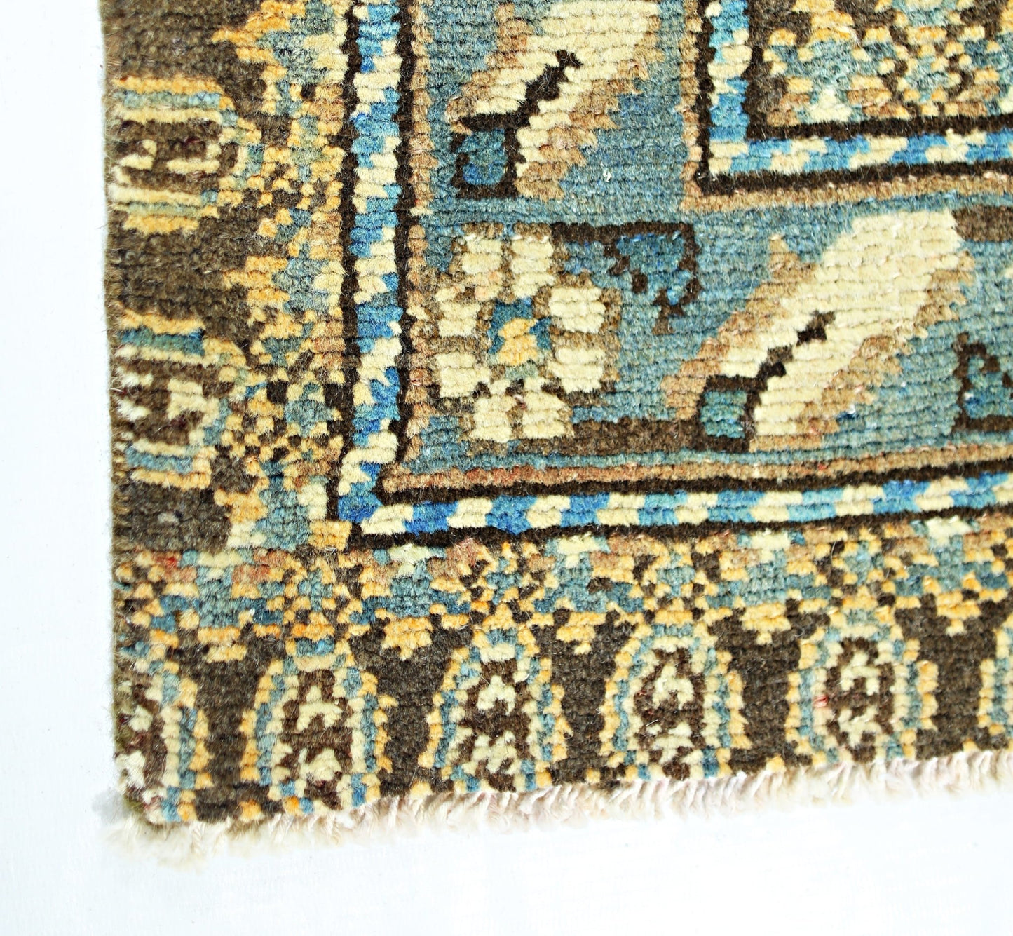 A corner detail of a vintage Persian Mazlaghan rug featuring geometric patterns in blue and brown.