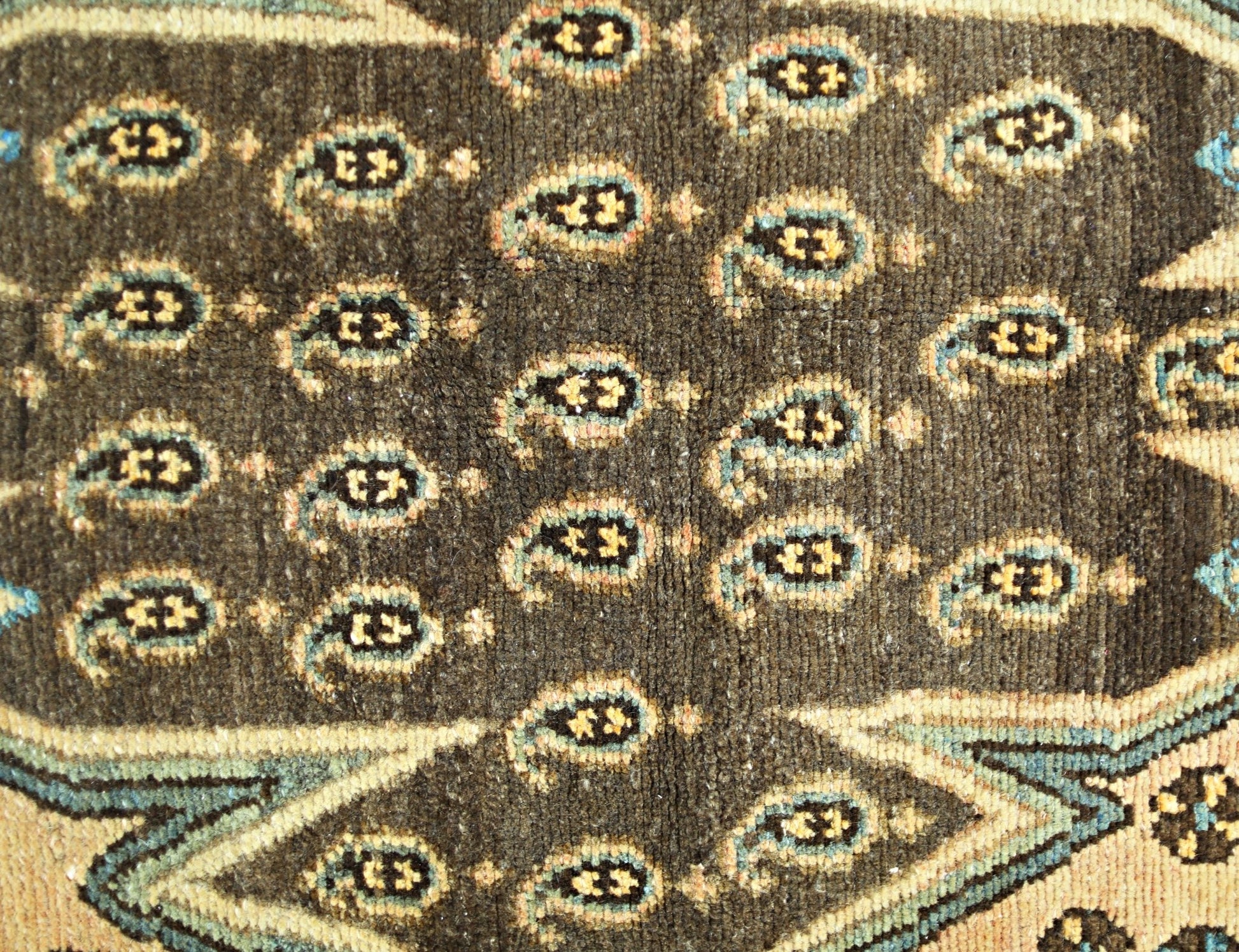 A close-up of a vintage Persian Mazlaghan rug featuring a dark brown field with repeating paisley.