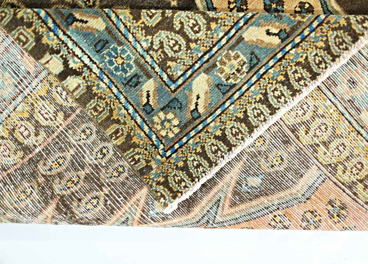 A folded vintage Persian Mazlaghan rug featuring intricate geometric patterns in blue, brown, and tan.