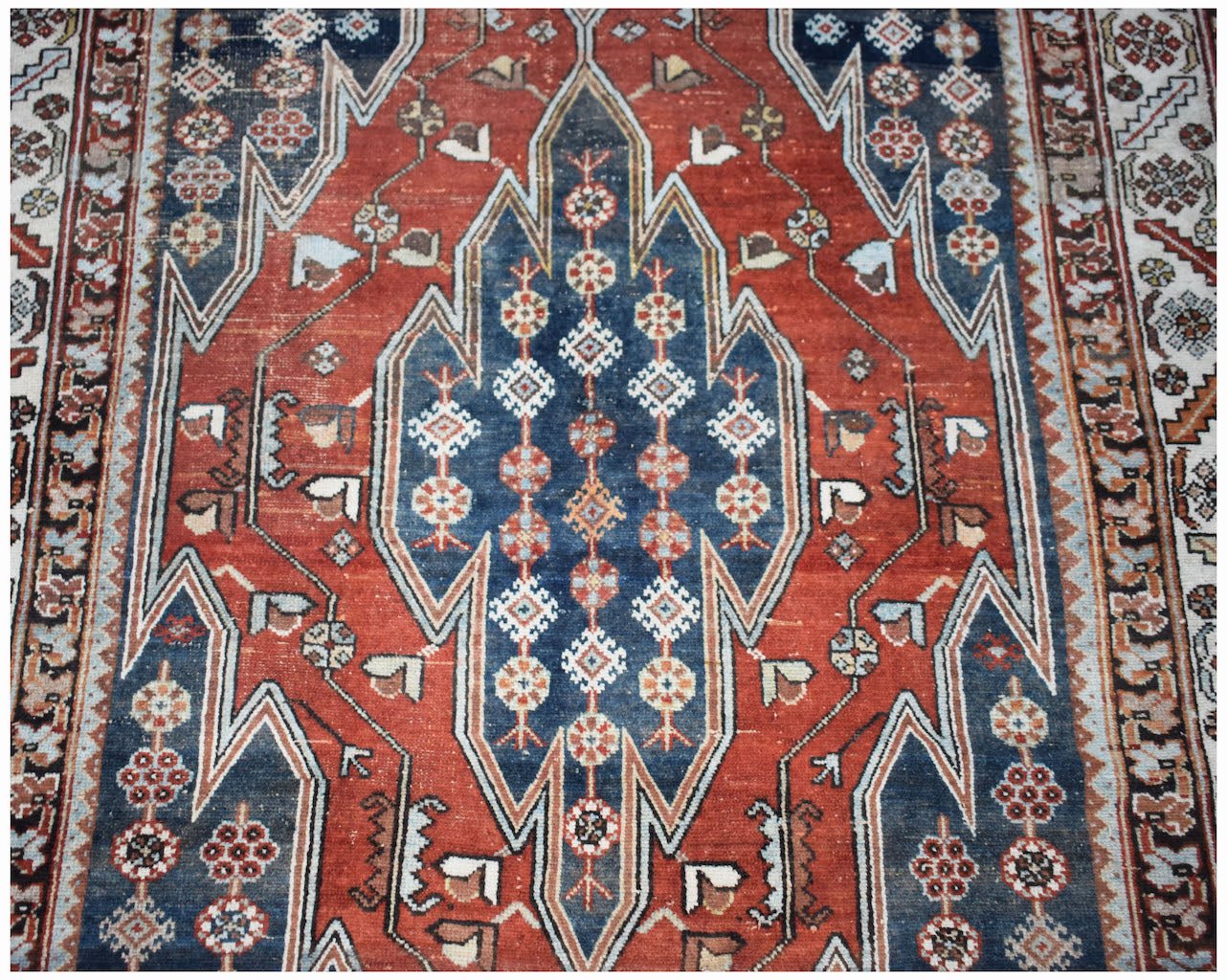 A vintage Persian Mazlaghan rug featuring a geometric blue medallion on a red field.