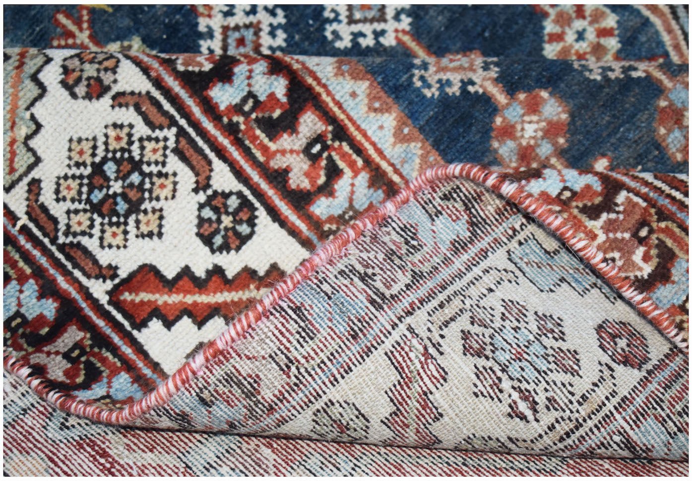 A corner of a vintage Persian Mazlaghan rug is folded back to show its wool pile and cotton base.