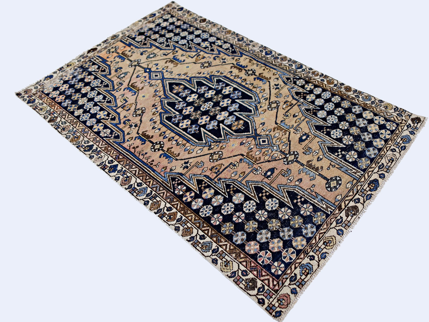 A vintage Persian Mazlaghan rug featuring a geometric medallion on a tan and navy blue field.