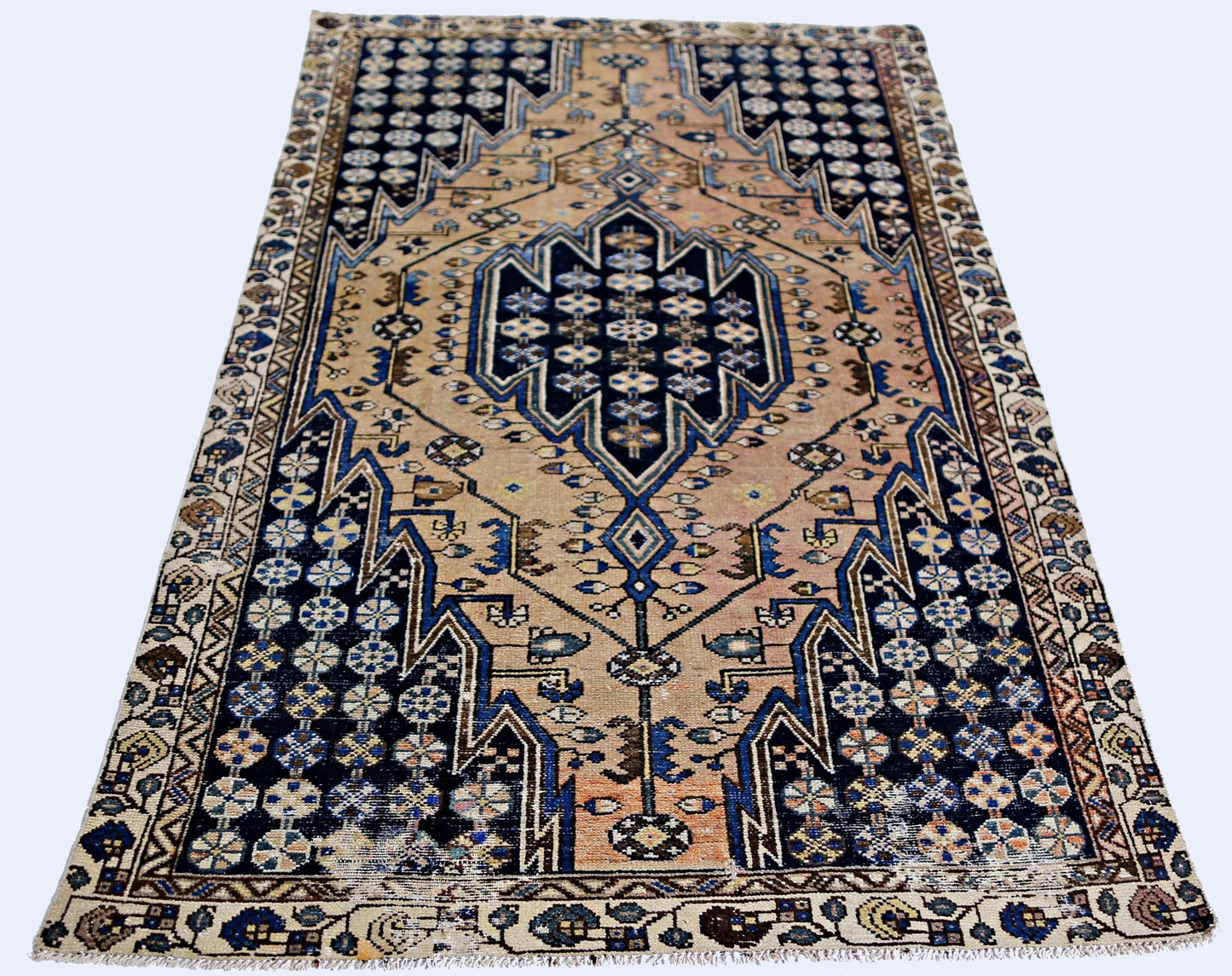 A vintage Persian Mazlaghan rug featuring a geometric blue medallion on a tan field.