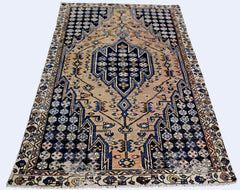 A vintage Persian Mazlaghan rug featuring a geometric blue medallion on a tan field.